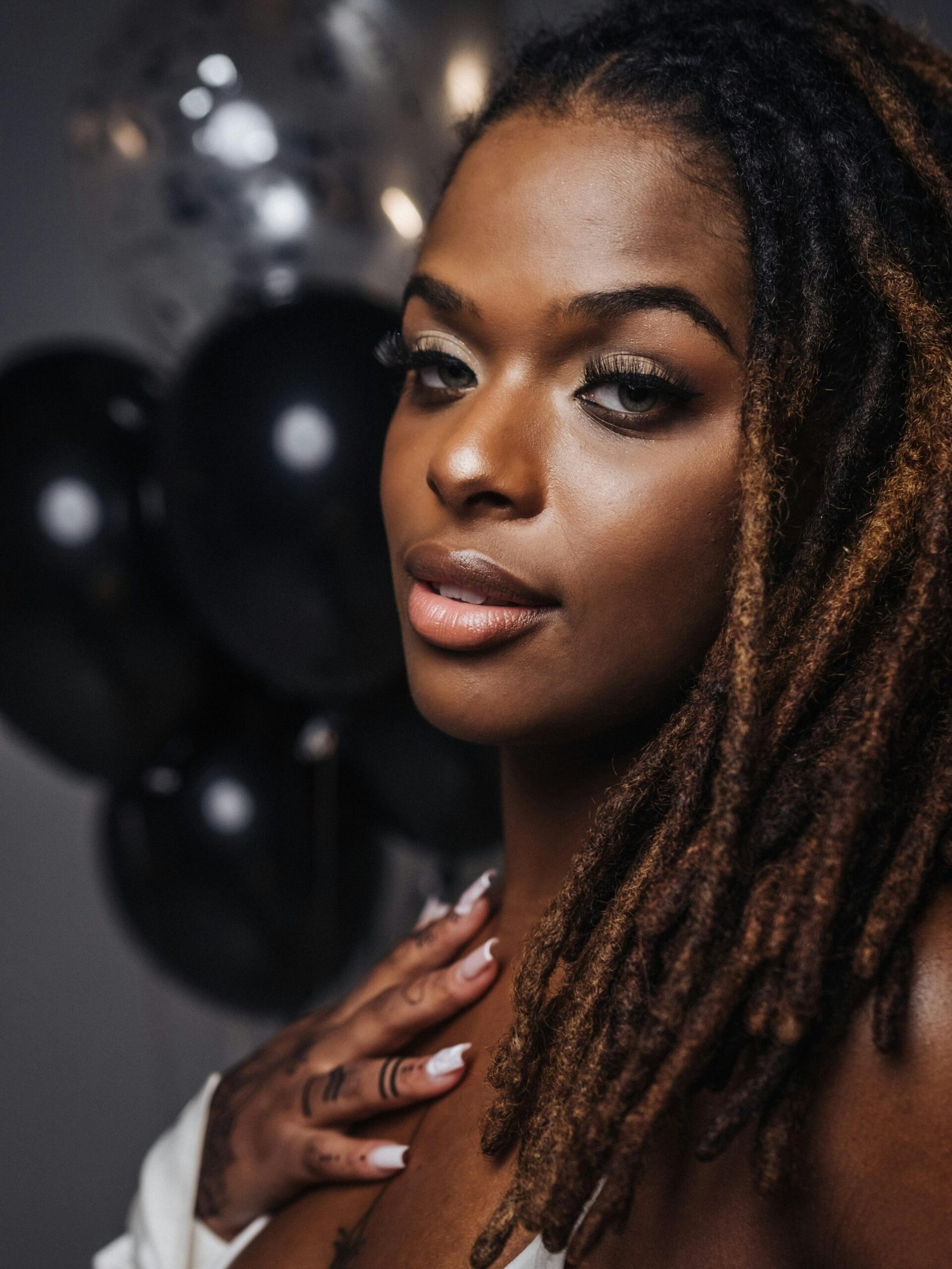 Captivating portrait of a woman with dreadlocks holding balloons indoors.
