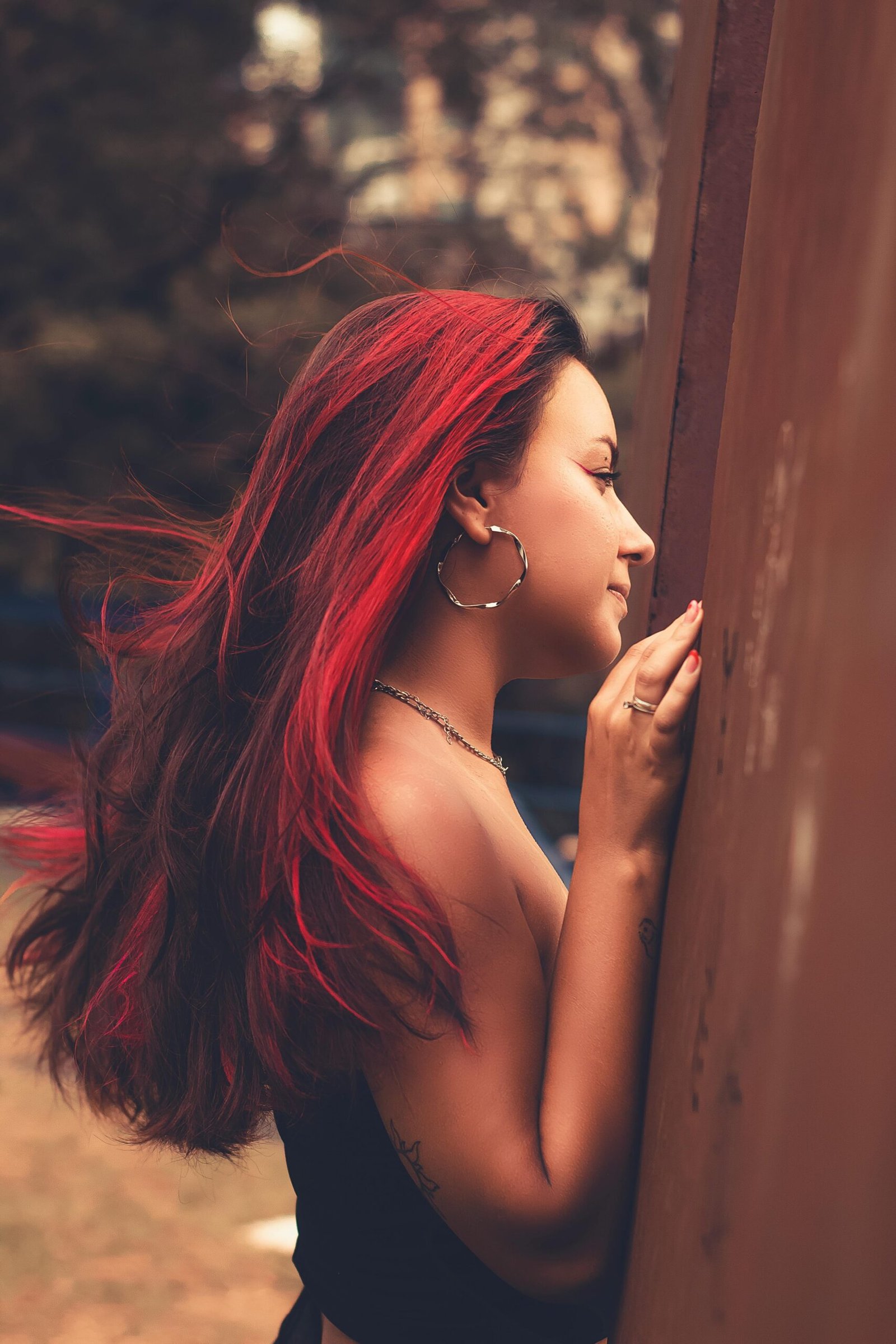 Portrait of a woman with red hair posing by a tree in a park, showcasing a stylish and modern look.