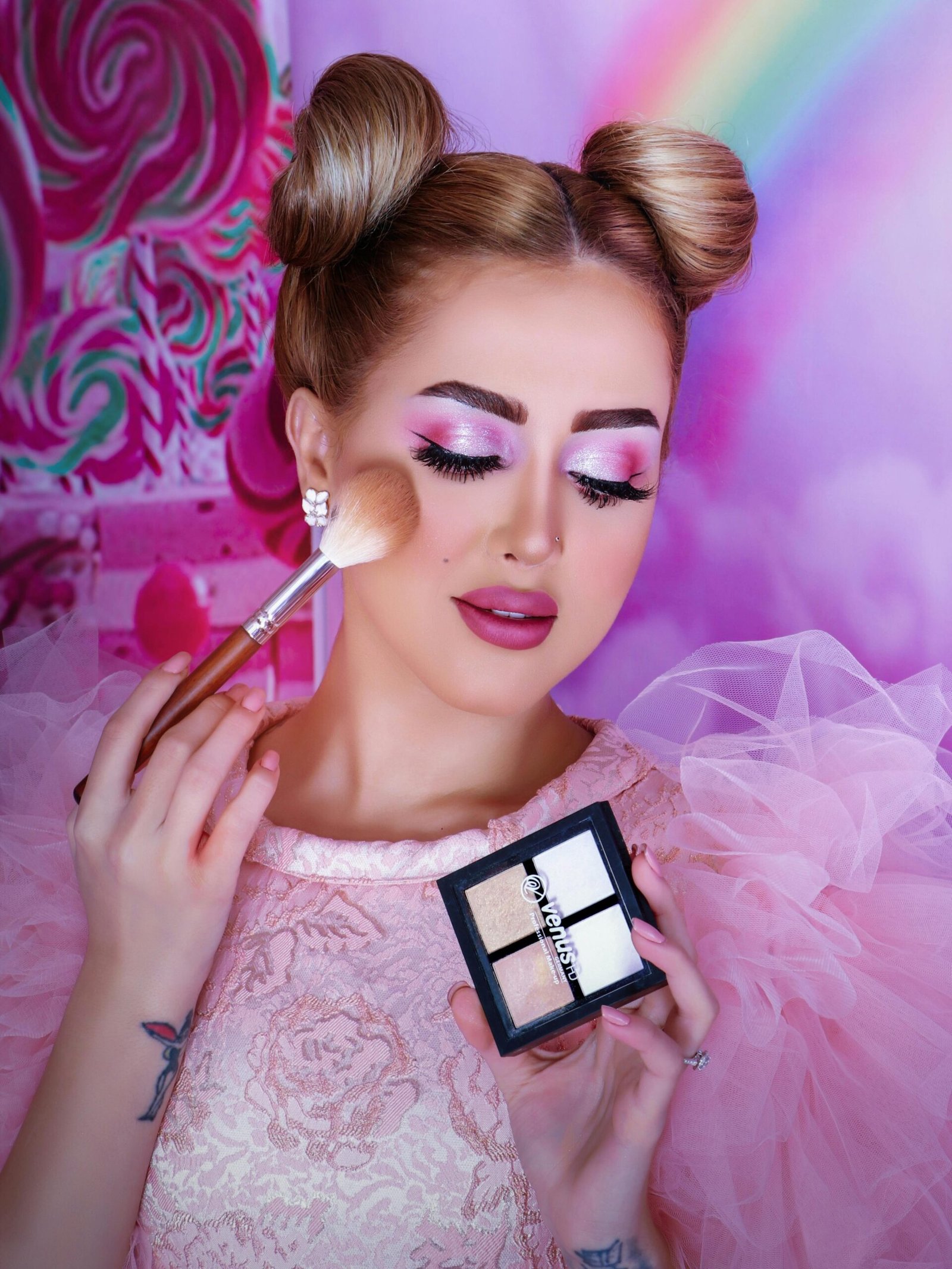 Vibrant portrait of a woman applying makeup with a pink theme and elegant hairstyle.