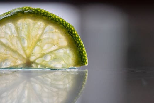 Detailed close-up of a lime slice showcasing its texture with a clear reflection on a smooth surface. limão