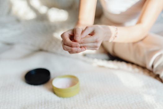 Close-up of a woman applying hand cream in a softly lit indoor setting, emphasizing skincare. unhas fracas