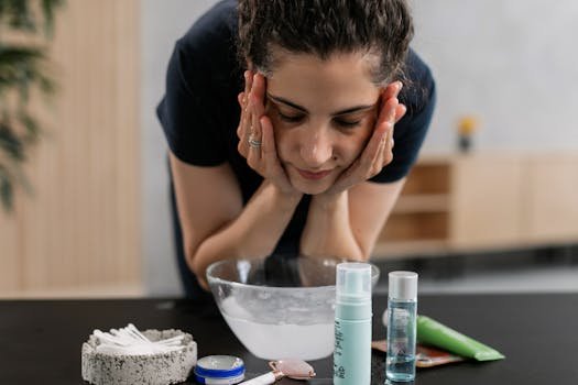 A woman performs her facial cleansing routine with various skincare products indoors. rosto