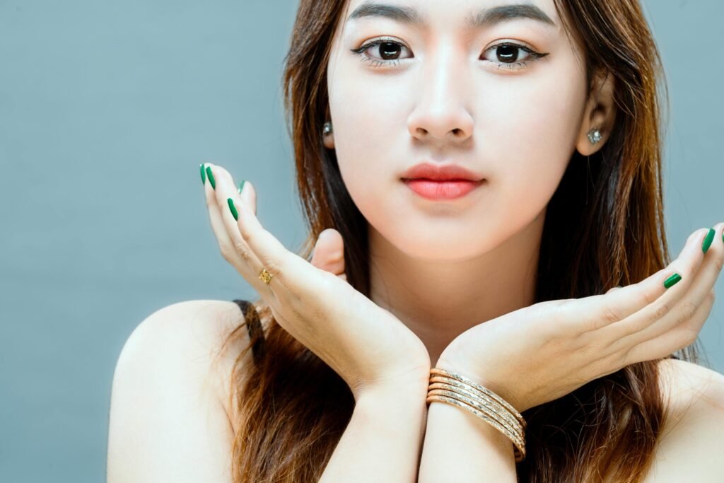 A close-up portrait showcasing a woman with long brown hair and hands under her chin against a white background.