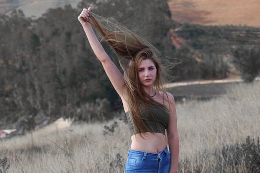 A young woman in a tube top and jeans poses in a rural Brazilian landscape, holding her hair aloft for a dynamic effect. cristalização