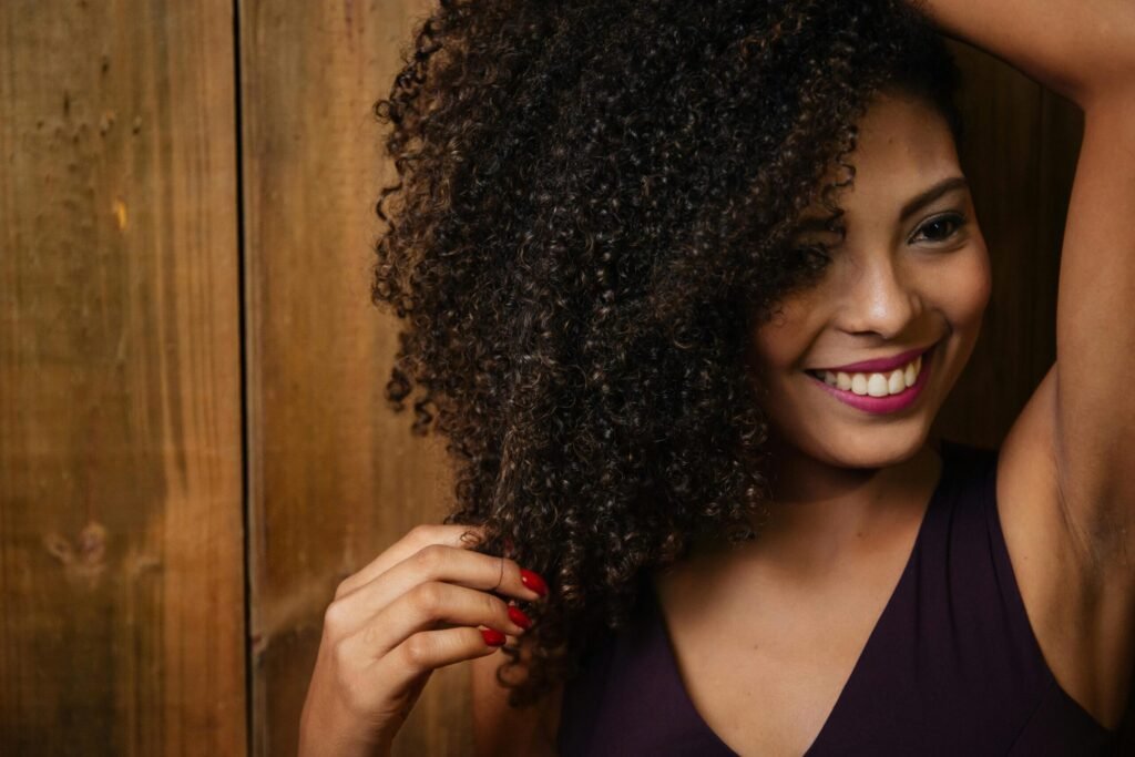 Close-up portrait of a smiling woman with curly hair touching her locks indoors.
