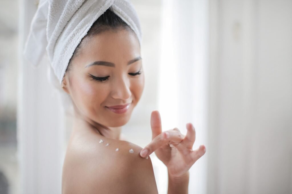 A young woman applying moisturizer indoors, enhancing skin care routine.