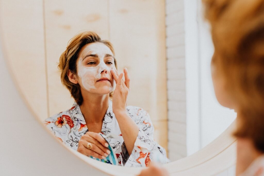 A woman applying a cosmetic mask for skincare in front of a mirror.